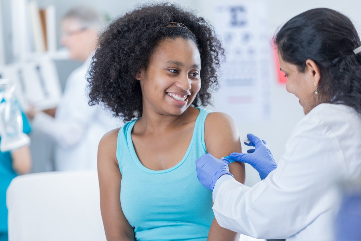 Female doctor puts a bandage on teenage girl's arm after receiving immunization.