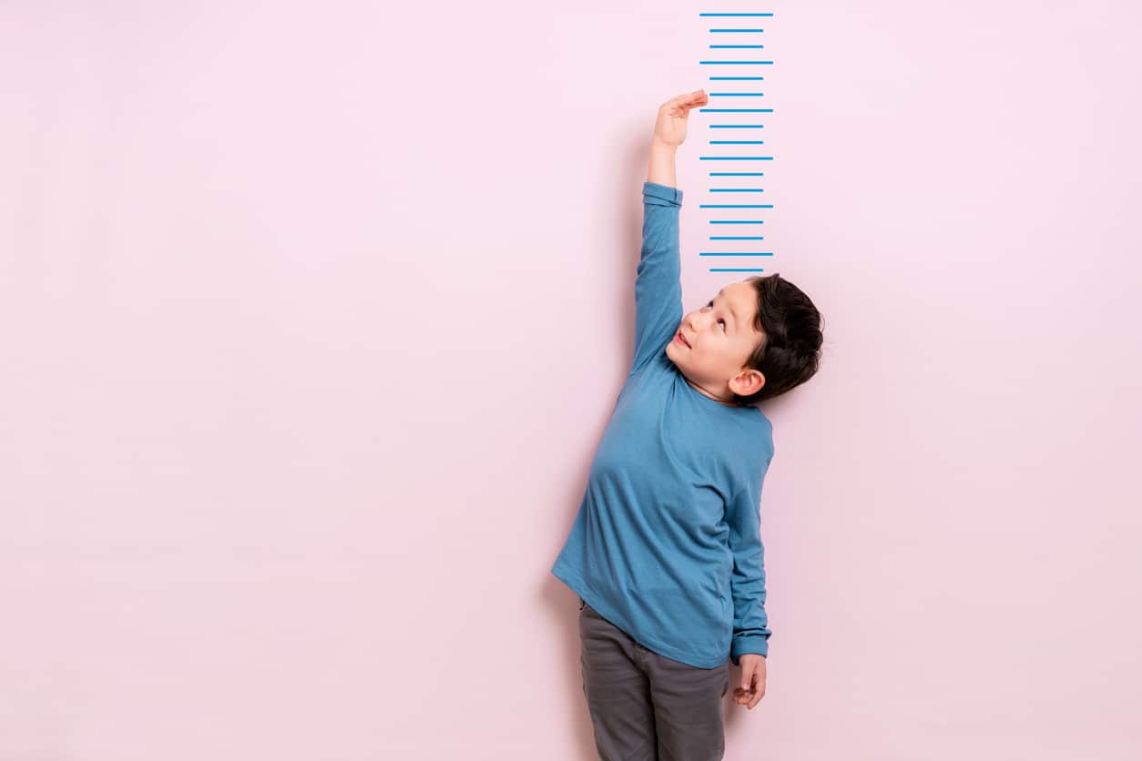 little boy standing in front of growth charts for kids with a pink background