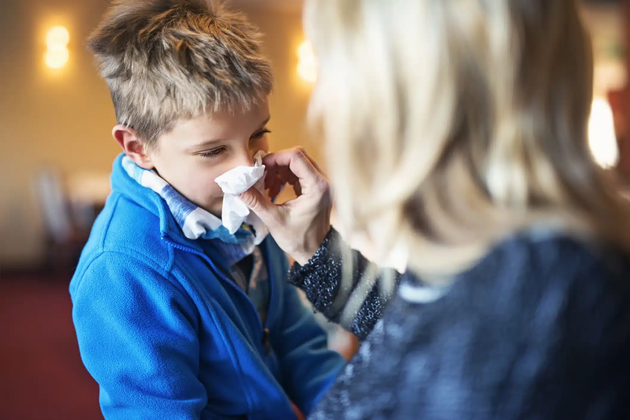 A mother helps her son stop a nosebleed with a tissue.